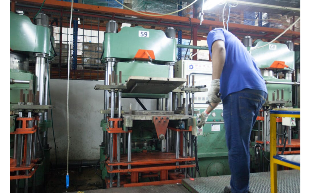 Factory operator loading a precision raw rubber preform into a heated mold cavity.