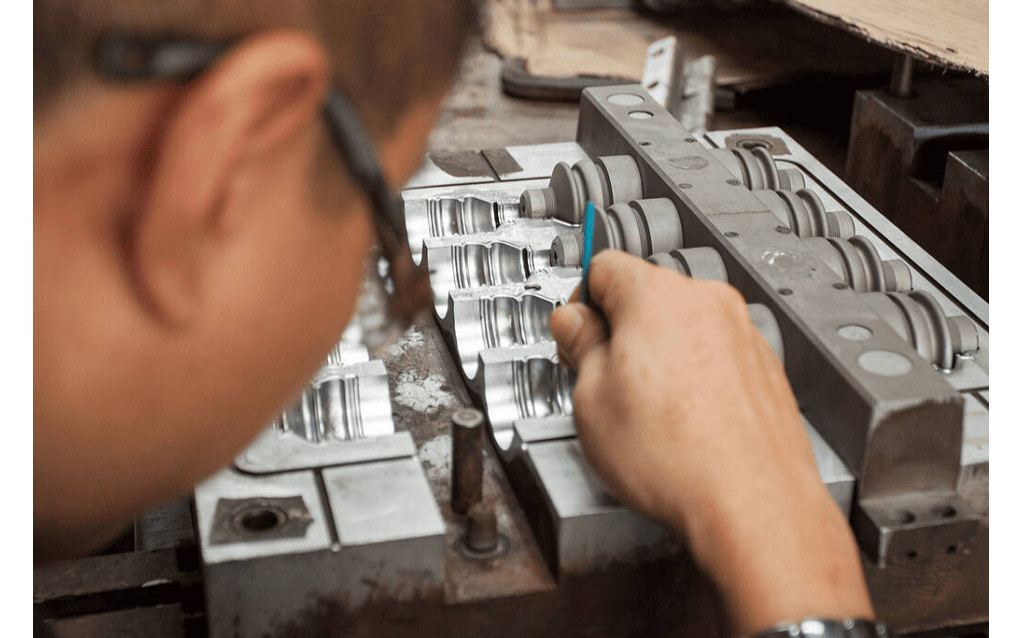 Expert toolmakers performing manual rubber mold maintenance, cleaning, and surface polishing at a workbench.